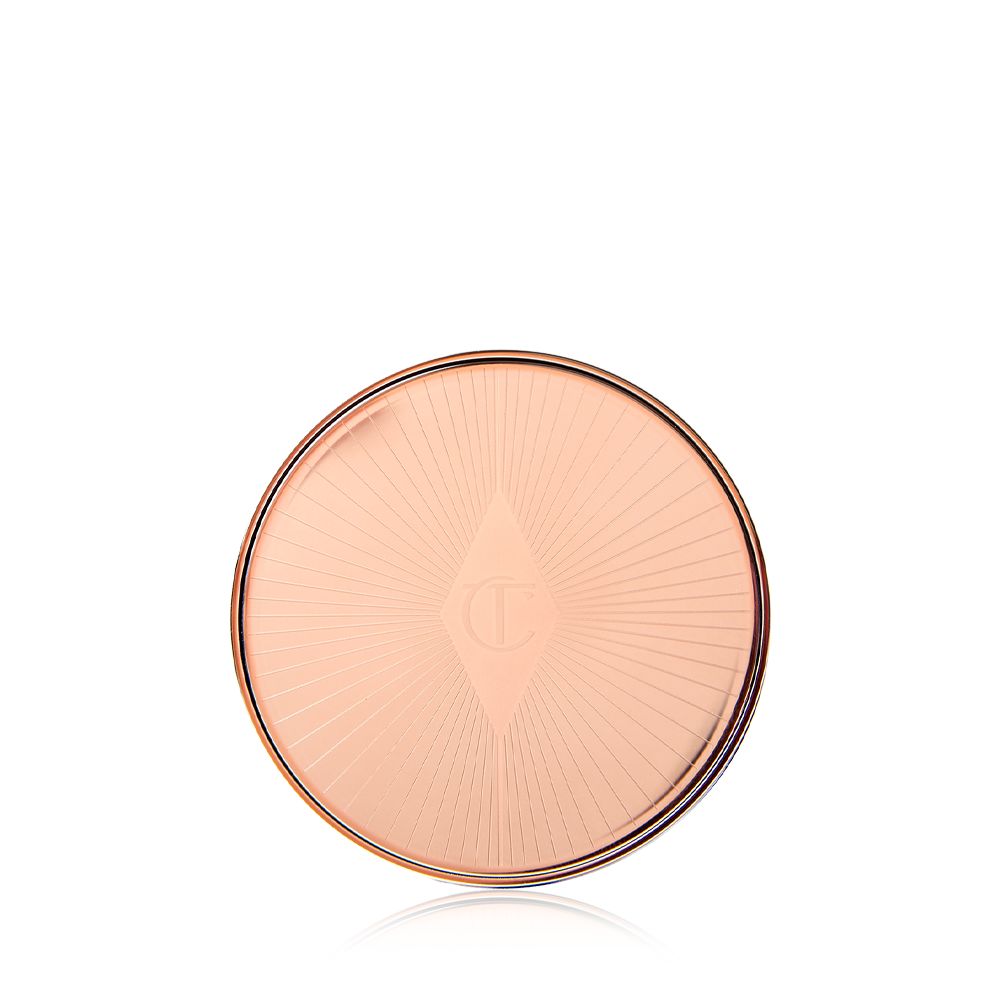 A closed lip and cheek cream product compact with rose gold packaging and a starburst pattern on the lid.