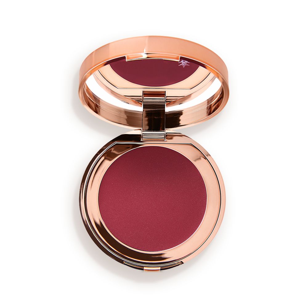 An open, mirrored-lid lip and cheek cream compact in a berry-red shade.