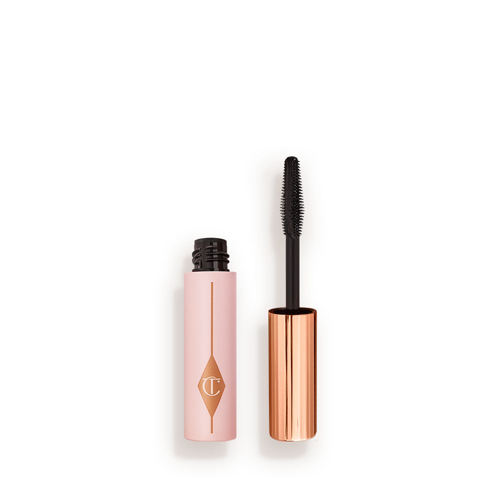 Travel-size mascara in a pink-coloured tube with its gold-coloured applicator next to it.