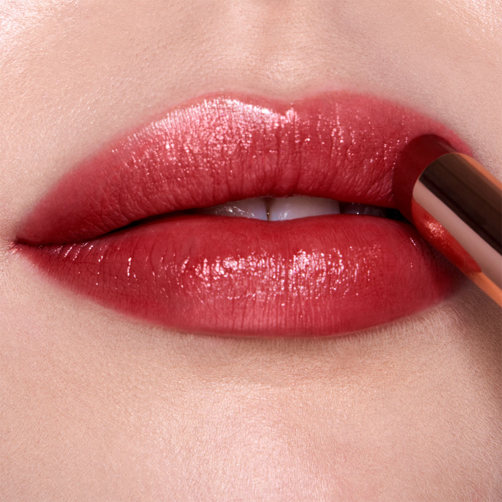Lips close-up of a fair-tone model applying a shimmery, sheer, berry-rose lipstick.