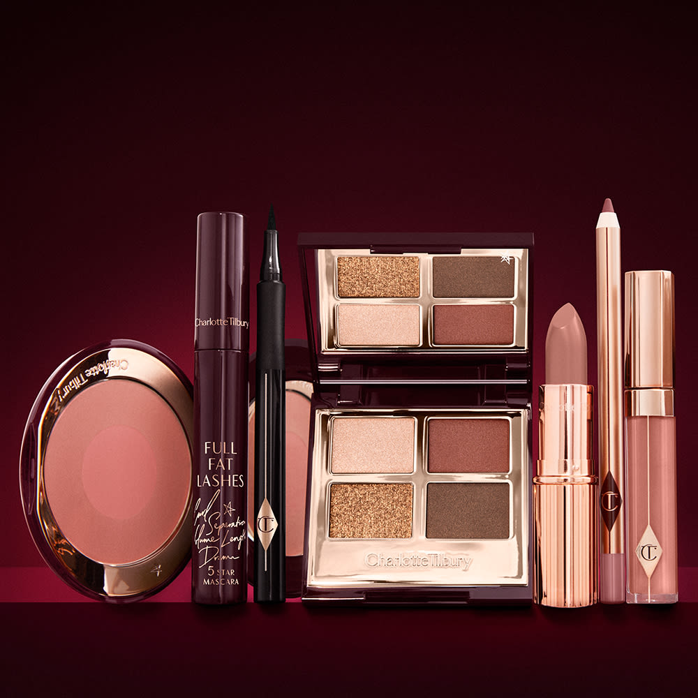 An open, mirrored-lid eyeshadow palette in matte and shimmery brown and gold shades, an open black eyeliner pen, a mascara in a dark-crimson colour scheme, a berry-rose lipstick with a matching lip liner pencil, nude pink lip gloss, and an open two-tone blush in warm pink.