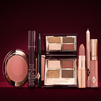 An open, mirrored-lid eyeshadow palette in matte and shimmery brown and gold shades, an open black eyeliner pen, a mascara in a dark-crimson colour scheme, a berry-rose lipstick with a matching lip liner pencil, nude pink lip gloss, and an open two-tone blush in warm pink.