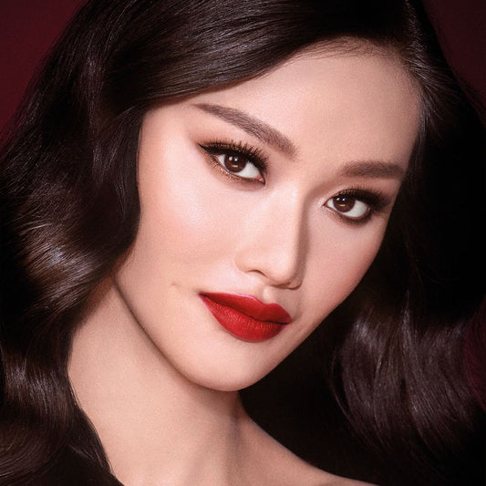 A fair-tone model with brown eyes wearing shimmery bronze eye makeup with muted pink blush and glossy scarlet-red lips