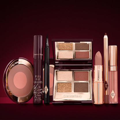 An open two-tone blush in cool-toned brown and warm pink with a mascara, eyeliner pen, quad eyeshadow palette with shimmery and matte brown and golden shades, an open lipstick in nude peach, lip liner pencil in taupe-brown, and a lip gloss in nude pink.