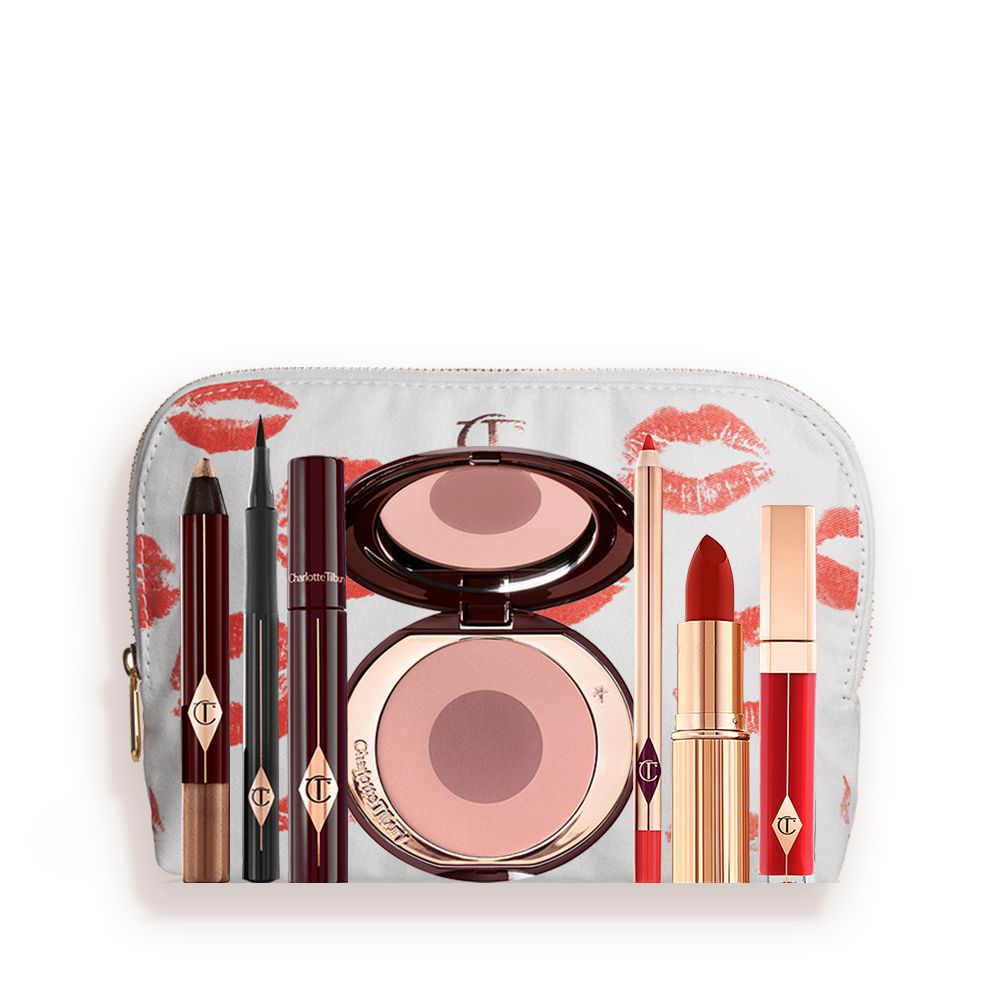 A white makeup pouch with an open two-tone blush in cool-toned pink and brown with a mascara, eyeliner pen, chubby eyeshadow stick in gold, an open lipstick in bold red, lip liner pencil in blood-red, and a lip gloss in bright red.