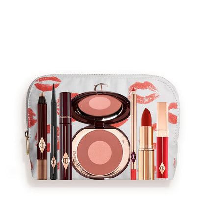 A white-coloured makeup pouch with an open two-tone blush in cool-toned terracotta and warm pink with a mascara, eyeliner pen, an open lipstick in bold red, lip liner pencil in blood-red, and a lip gloss in bright red.