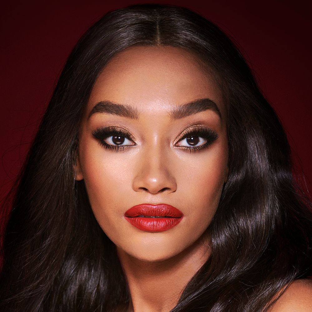 A deep-tone model with brown eyes wearing shimmery bronze eye makeup with muted pink blush and glossy scarlet-red lips