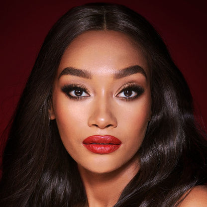 A deep-tone model with brown eyes wearing shimmery bronze eye makeup with muted pink blush and glossy scarlet-red lips