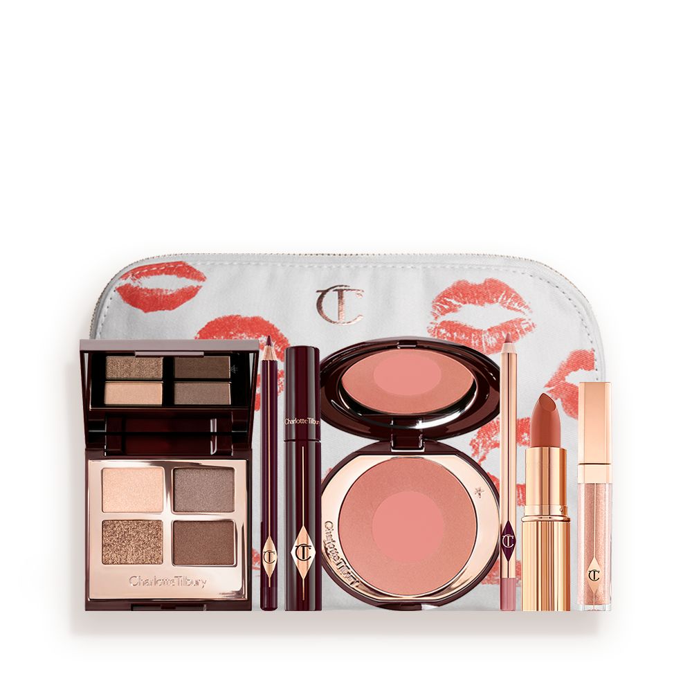 An open, mirrored-lid eyeshadow palette in matte and shimmery gold, brown, and beige shades, an open black eyeliner pencil, a mascara in a dark-crimson colour scheme, a golden-peach lipstick with a nude pink lip liner pencil, nude-peach lip gloss, and an open two-tone blush in muted brown-pink.