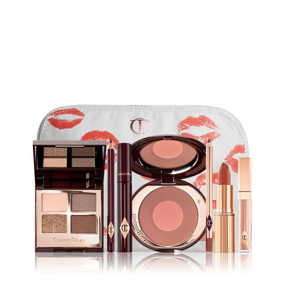 An open, mirrored-lid eyeshadow palette in matte and shimmery gold, brown, and beige shades, an open black eyeliner pencil, a mascara in a dark-crimson colour scheme, a burnt orange lipstick with a matching lip liner pencil, nude-peach lip gloss, and an open two-tone blush in medium brown-pink.