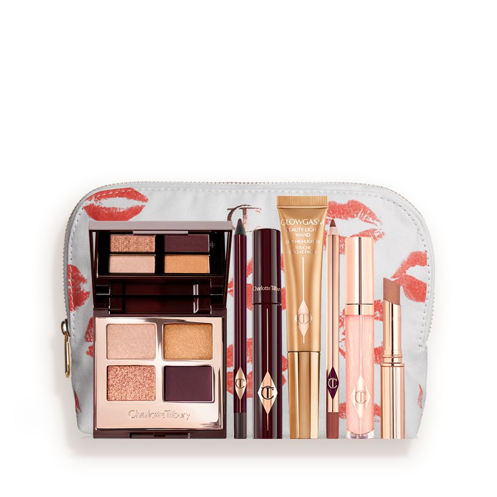 A highlighter wand in a honey-gold-coloured tube with a mascara, eyeliner pencil, quad eyeshadow palette with shimmery and matte rose gold, plum, and golden shades, an open lipstick in nude brown, lip liner pencil in soft plum, and a lip gloss in nude pink, and a white-coloured makeup pouch.