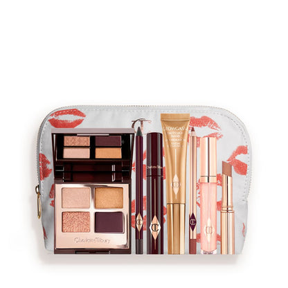A highlighter wand in a honey-gold-coloured tube with a mascara, eyeliner pencil, quad eyeshadow palette with shimmery and matte rose gold, plum, and golden shades, an open lipstick in nude brown, lip liner pencil in soft plum, and a lip gloss in nude pink, and a white-coloured makeup pouch.