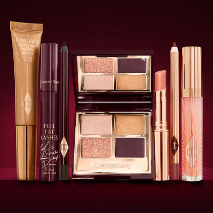 A highlighter wand in a honey-gold-coloured tube with a mascara, eyeliner pencil, quad eyeshadow palette with shimmery and matte rose gold, plum, and golden shades, an open lipstick in nude coral, lip liner pencil in soft plum, and a lip gloss in nude pink.