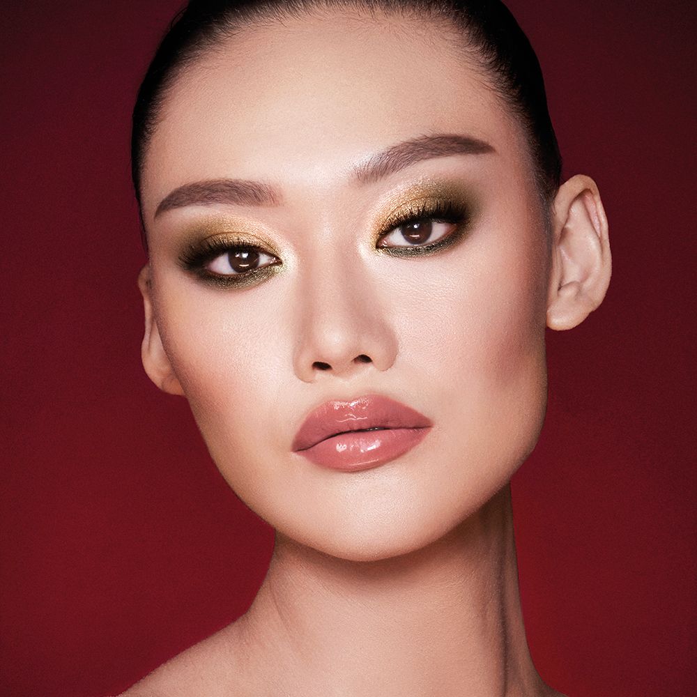 A fair-tone model with brown eyes wearing smokey green eye makeup with black eyeliner, soft brown blush, and nude pink lipstick topped up with gloss.