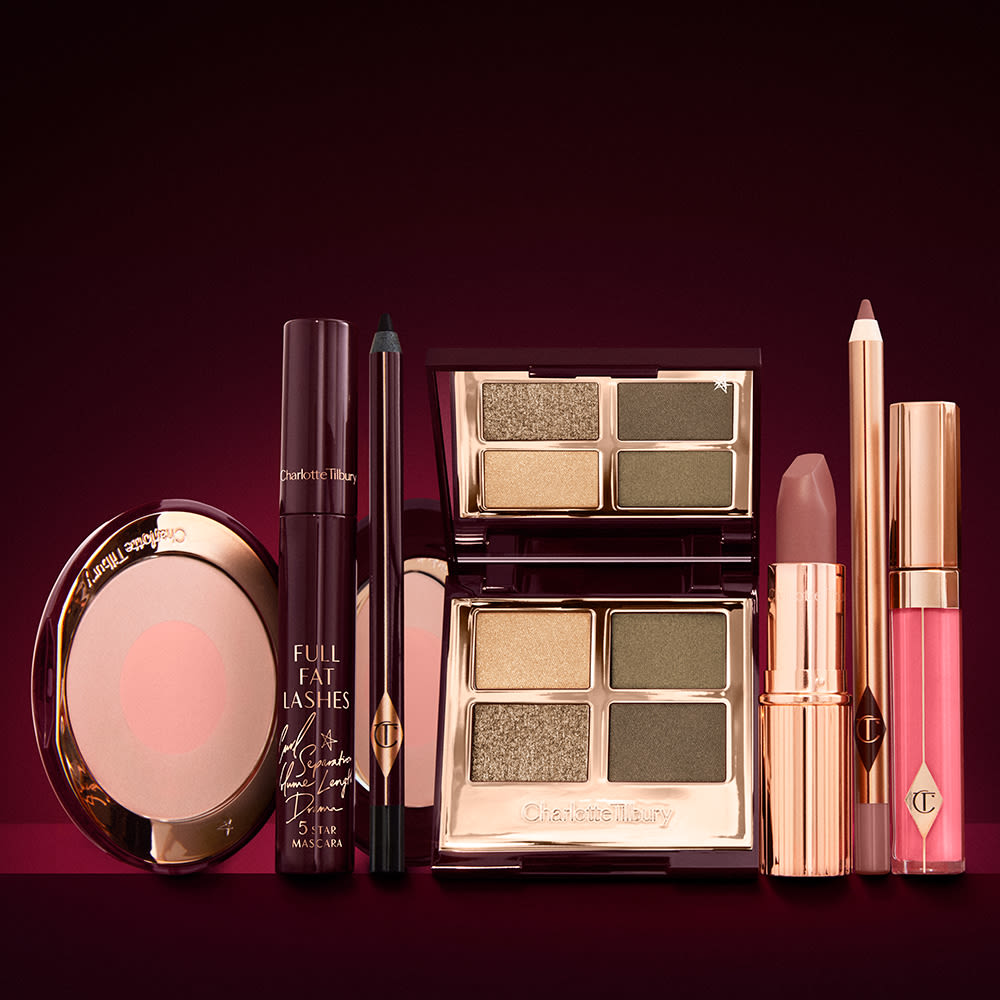 A quad eyeshadow palette in shades of green and gold, a brown eyeliner pencil, mascara, an open two-tone blush in nude pink, a warm pink lip liner pencil, a warm rose lipstick, and a bright pink lip gloss.