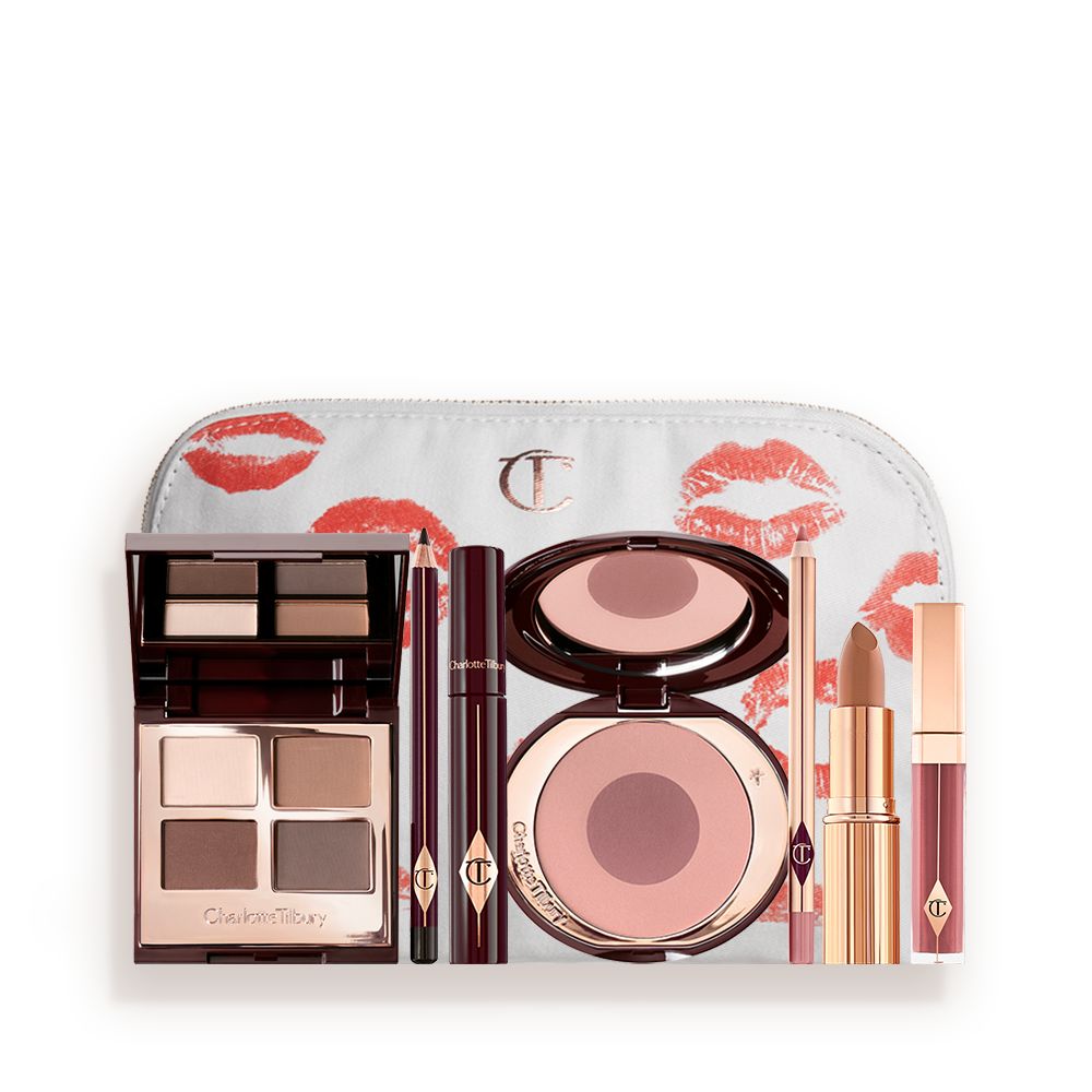A makeup bag with 7 makeup products, which are a quad eyeshadow palette in shades of champagne, gold, and bronze, a dark brown eyeliner pencil, mascara, a two-tone brown and pink powder blush, tawny-brown lip liner, a terracotta lipstick, and a deep pinkish-red lip gloss.