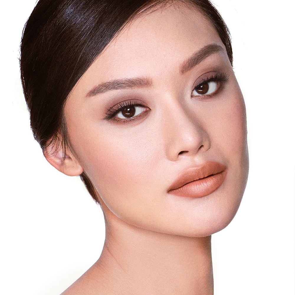 A fair-tone model with brown eyes wearing smokey brown eye makeup with muted pink blush with glossy soft-brown lips.