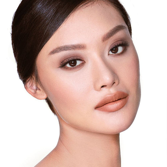 A fair-tone model with brown eyes wearing smokey brown eye makeup with muted pink blush with glossy soft-brown lips.