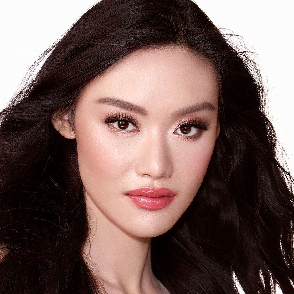 A fair-tone model with brown eyes wearing shimmery rose gold and brown eye makeup with brown eyeliner, soft pink blush, and coral-pink lipstick with gloss on top.