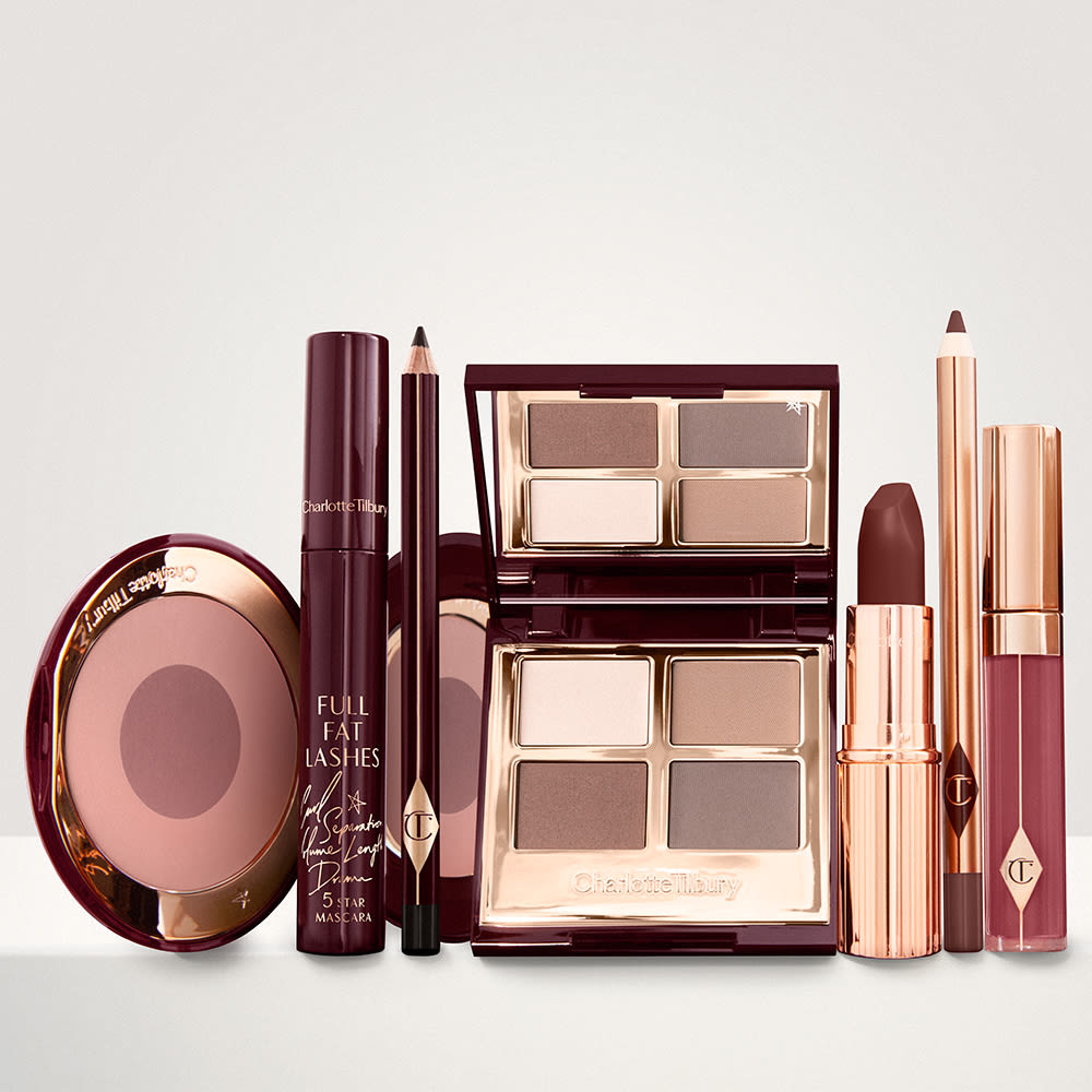 A quad eyeshadow palette in shades of champagne, gold, and bronze, a dark brown eyeliner pencil, mascara, a two-tone brown and pink powder blush, tawny-brown lip liner, a maroon lipstick, and a warm pinkish-red lip gloss.