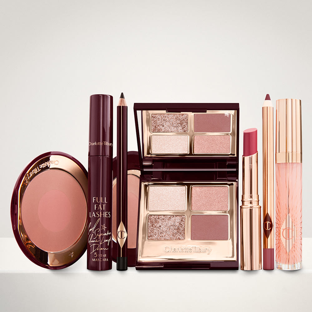 An open two-tone blush in cool-toned brown and warm pink with a mascara, eyeliner pencil, quad eyeshadow palette with shimmery and matte brown and golden shades, an open lipstick in nude red, lip liner pencil in maroon and a lip gloss in nude pink.