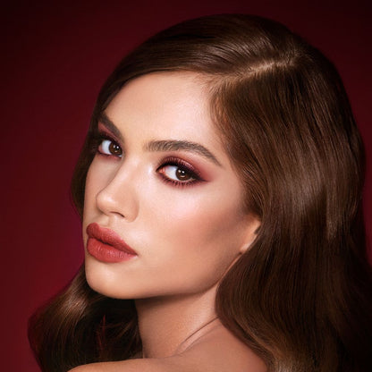 A medium-tone brunette model with reddish-plum eye makeup, glowy face base, and a vampy-red lipstick with a satin-finish.