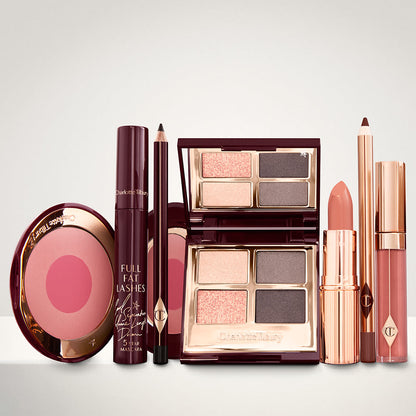 An open two-tone blush in cool-toned pink and fuchsia with a mascara, eyeliner pencil, quad eyeshadow palette with shimmery and matte grey and golden shades, an open lipstick in nude red, lip liner pencil in taupe-brown, and a lip gloss in warm brown-peach.