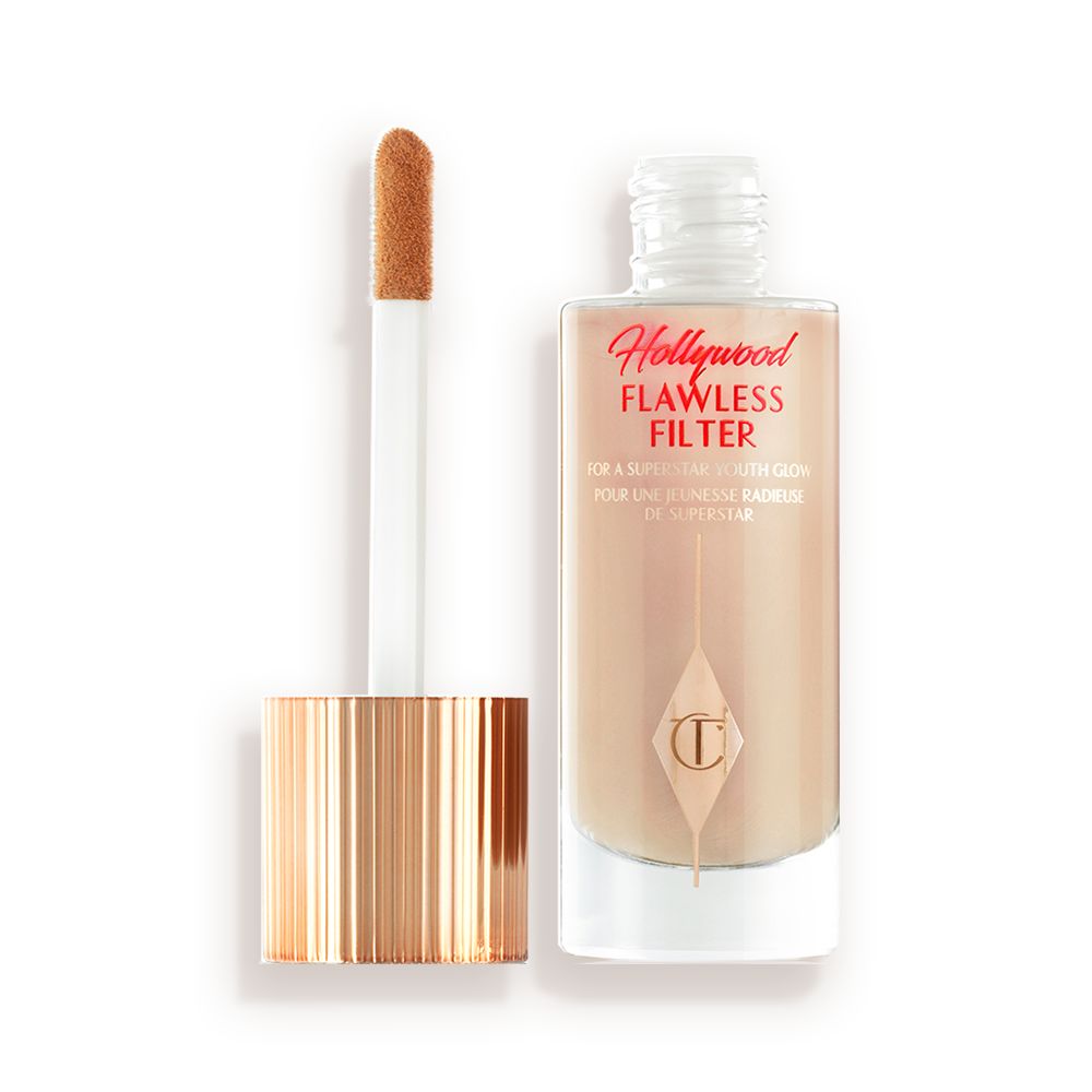 An open, luminous primer in a light cool-toned-beige shade in a glass bottle with its gold and white doe-foot applicator next to it.