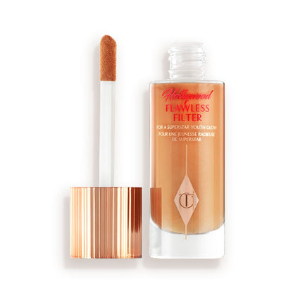 An open, luminous primer in a medium golden-beige shade in a glass bottle with its gold and white doe-foot applicator next to it.