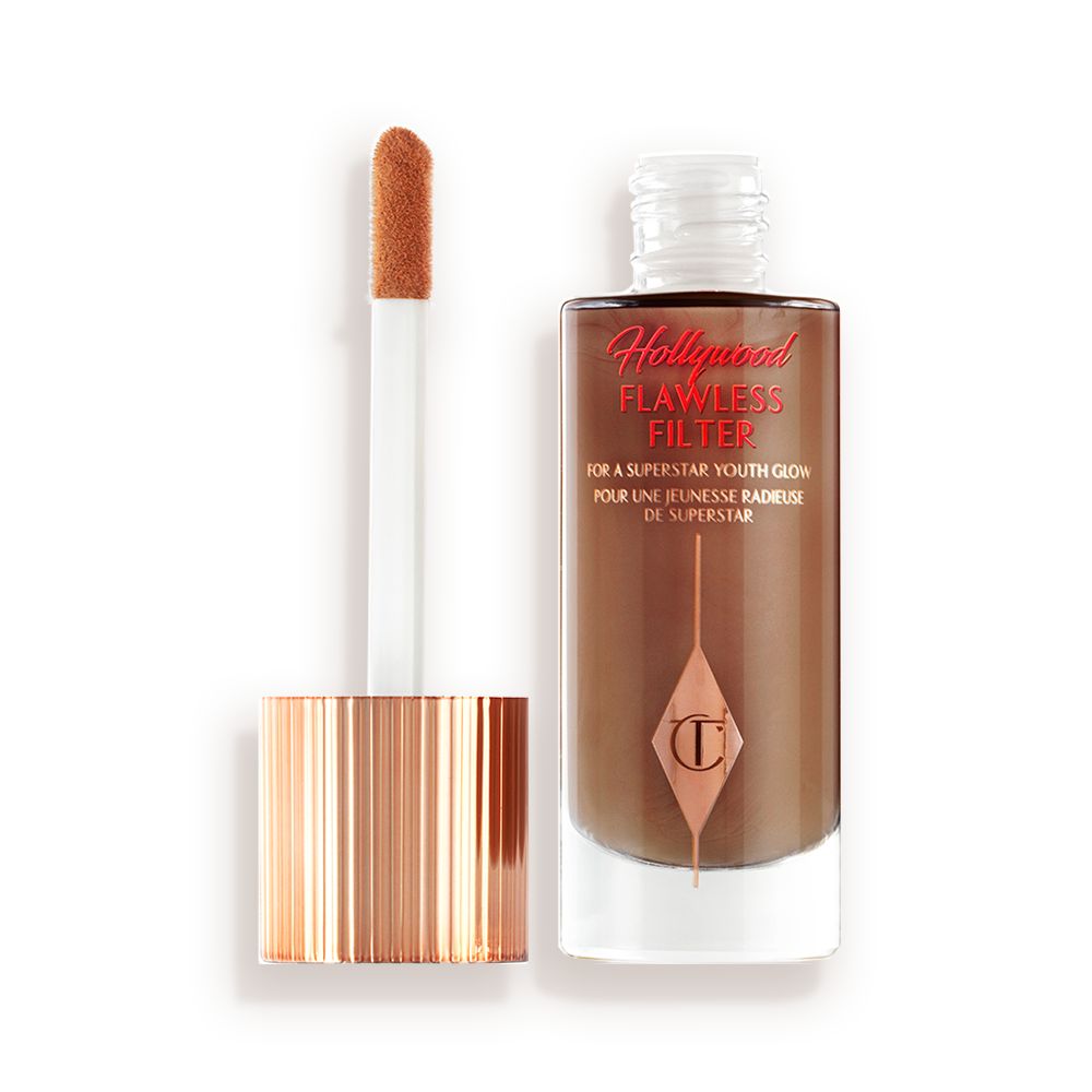 An open, luminous primer in a dark brown shade in a glass bottle with its gold and white doe-foot applicator next to it.